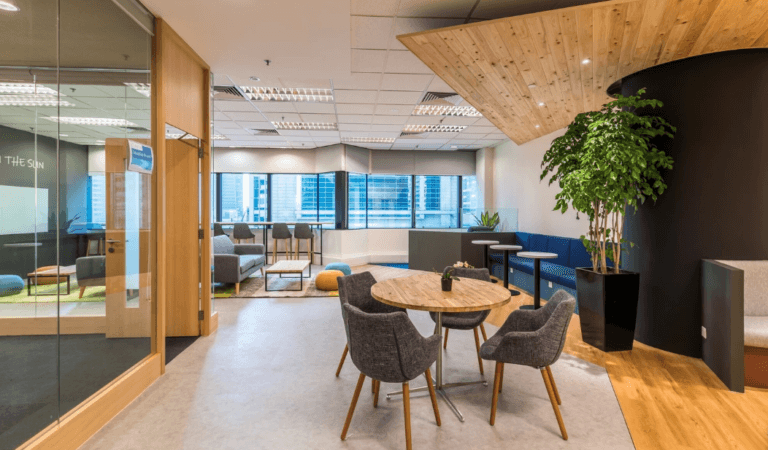 Stylish office lounge with wooden ceiling, cozy seating, indoor plants, and city views through large windows