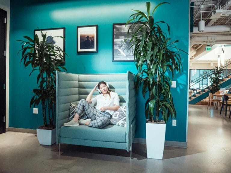 A woman relaxing on a modern high-back sofa in a stylish coworking space with vibrant teal walls and plants