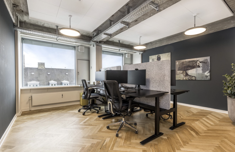 Contemporary office with ergonomic chairs, dual monitors, wood flooring, and large exterior windows