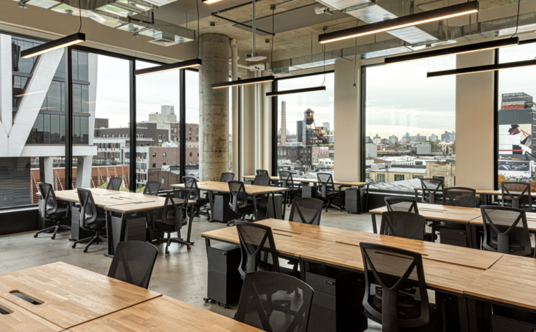 Spacious modern coworking office with natural light and city skyline view through large windows.