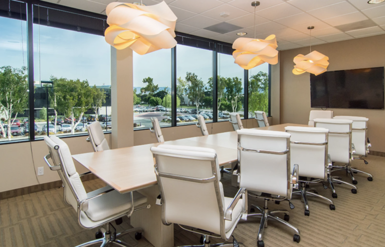 Modern conference room with large windows, white chairs, natural light, and decorative pendant lights